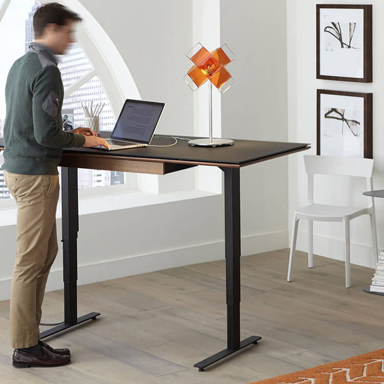 Homme debout sur un bureau réglable pour une configuration de travail ergonomique.